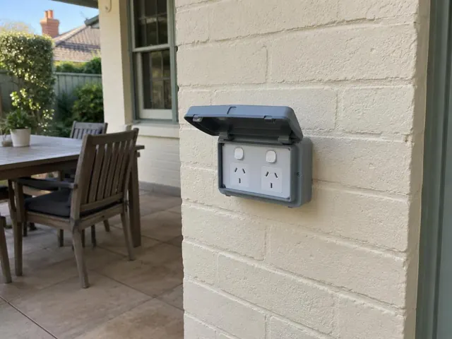 Outdoor double power point with weatherproof cover on a rendered brick wall beside a patio in Lambton